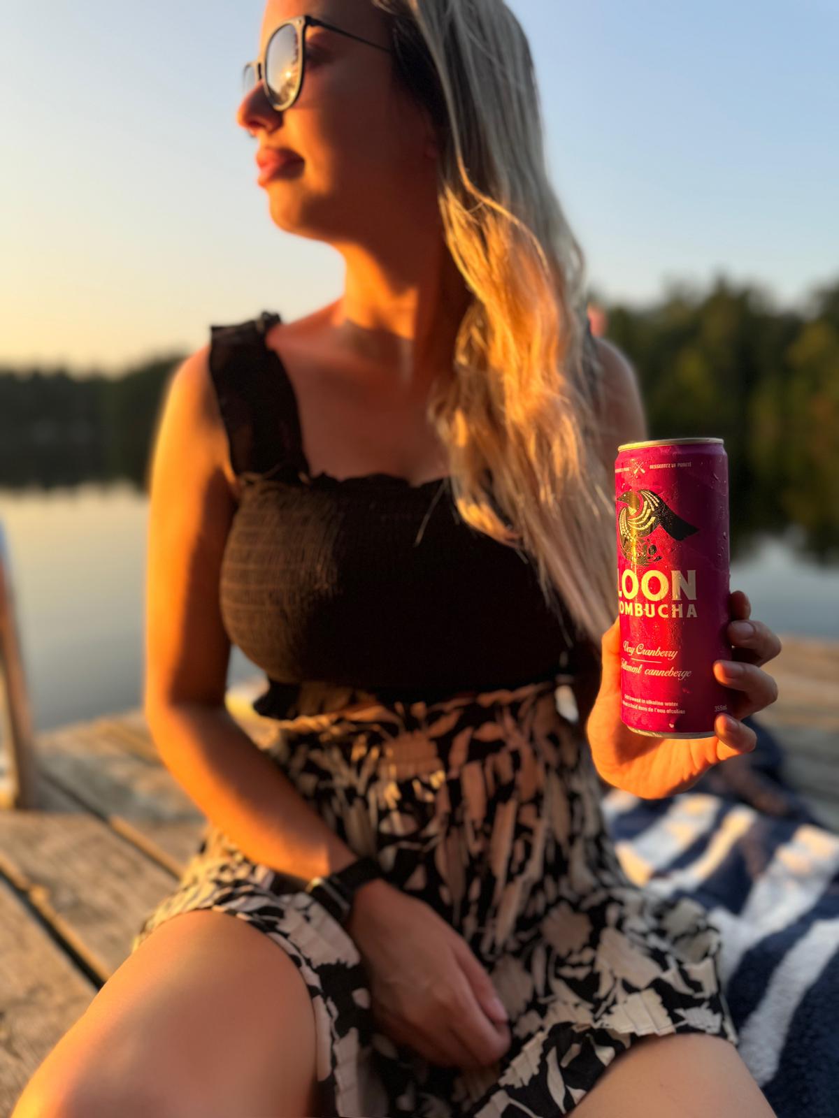 Woman holding kombucha can at sunset